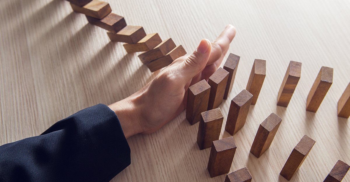 Hand stopping wooden dominoes from falling 